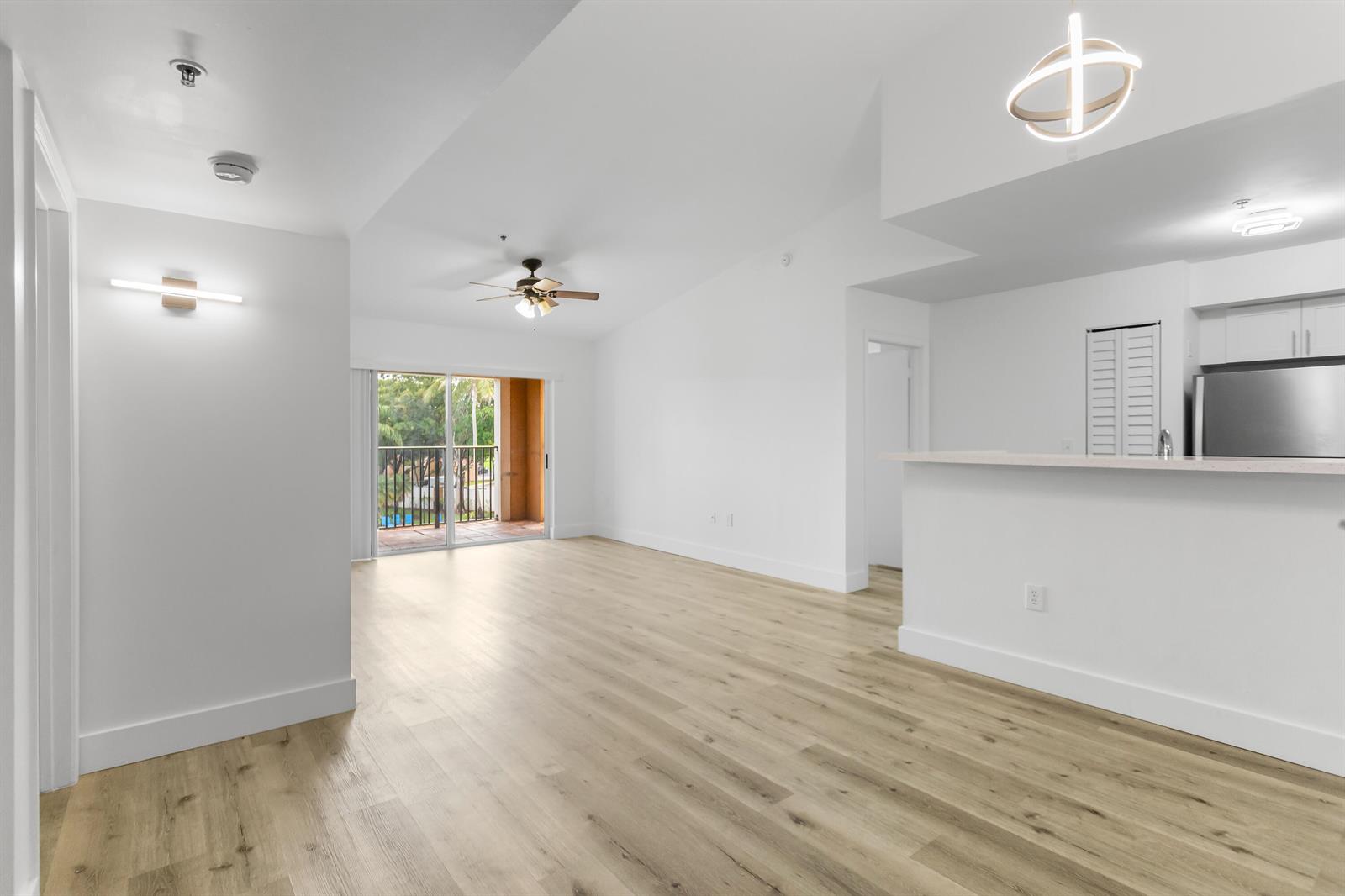 An open-concept living area features light wood-look flooring, white walls, and a sliding glass door — 2113 Renaissance Boulevard # 306, Miramar FL 33025, MIRAMAR, FL