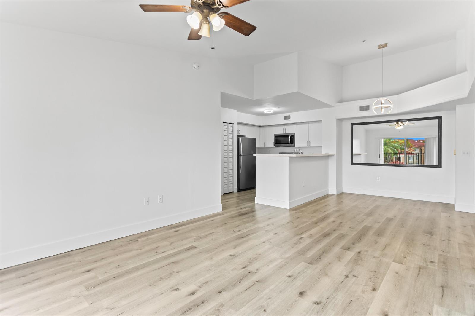 An open-concept living area features light wood-look flooring, a ceiling fan, and a kitchen — 2113 Renaissance Boulevard # 306, Miramar FL 33025, MIRAMAR, FL