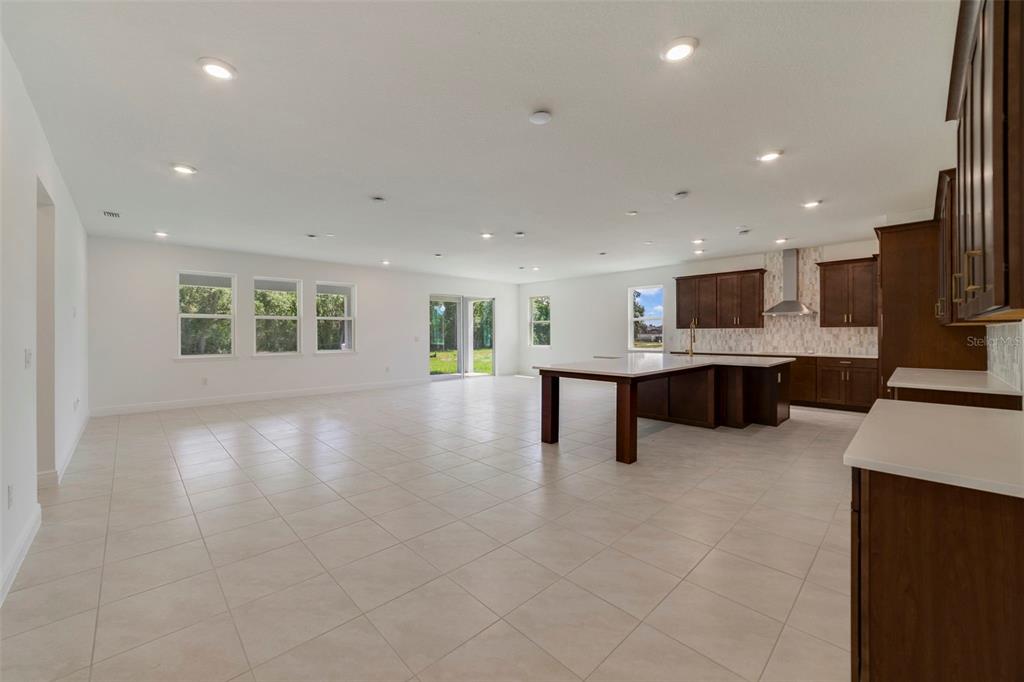 A spacious open-concept kitchen and living area with tile flooring, dark cabinetry, and recessed lighting — 3057 WATER CLOVER COURT, APOPKA, FL