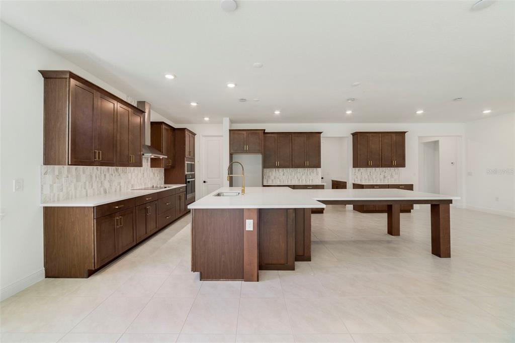 A modern kitchen features dark wood cabinets, white countertops, a large island, and tile flooring — 3057 WATER CLOVER COURT, APOPKA, FL