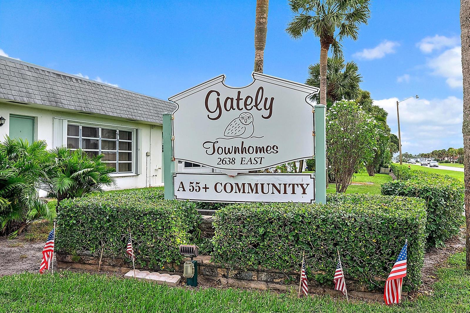 A sign for Gately Townhomes stands in front of a hedge with several small flags — 2638 Gately Drive E # 45, West Palm Beach FL 33415, WEST PALM BEACH, FL
