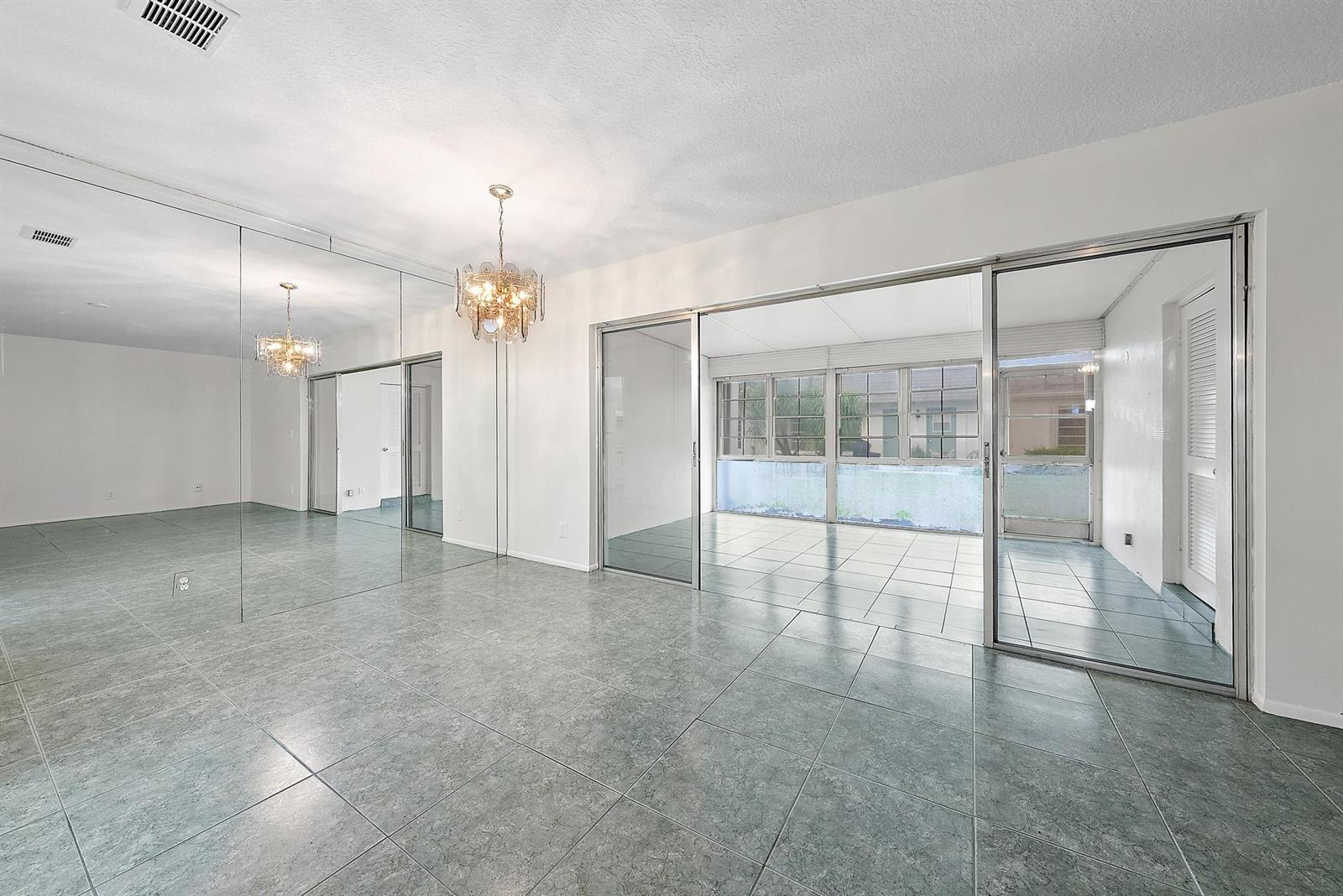 A room with gray tile flooring, a mirrored wall, a chandelier, and sliding glass doors — 2638 Gately Drive E # 45, West Palm Beach FL 33415, WEST PALM BEACH, FL