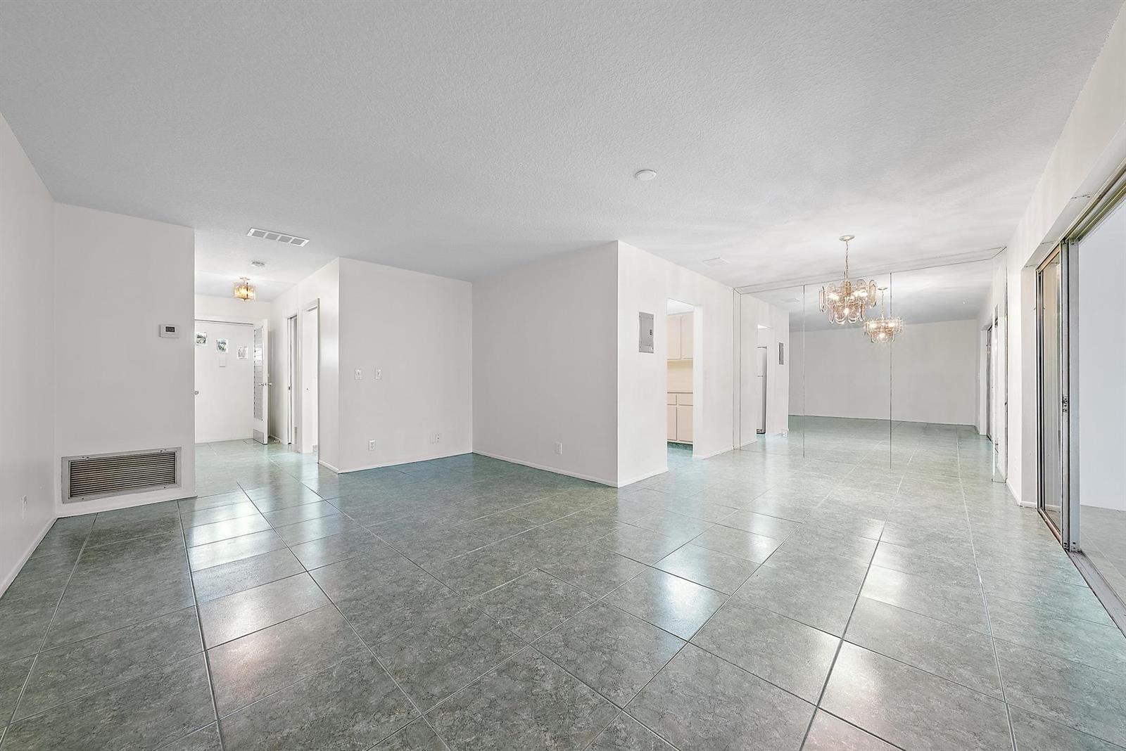 An empty room with white walls, gray tile flooring, a mirrored wall, and a chandelier — 2638 Gately Drive E # 45, West Palm Beach FL 33415, WEST PALM BEACH, FL