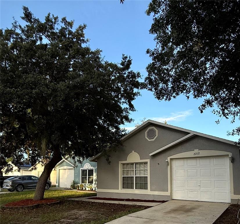 A gray single-story house with a white garage door and a large tree in front — 2212 ROSE BROOK COURT, ORLANDO, FL