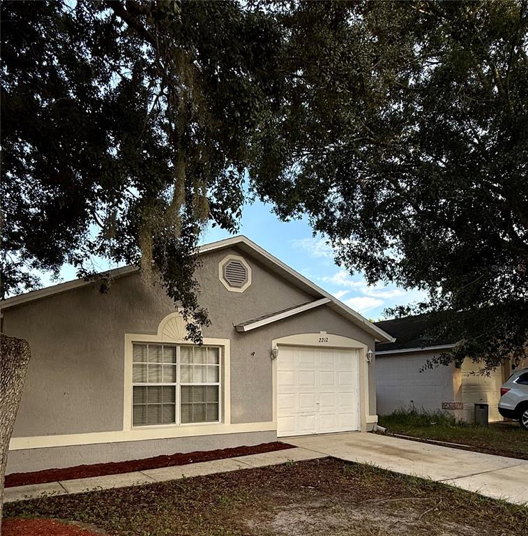 A single-story gray house with a white garage door and a large tree in front — 2212 ROSE BROOK COURT, ORLANDO, FL