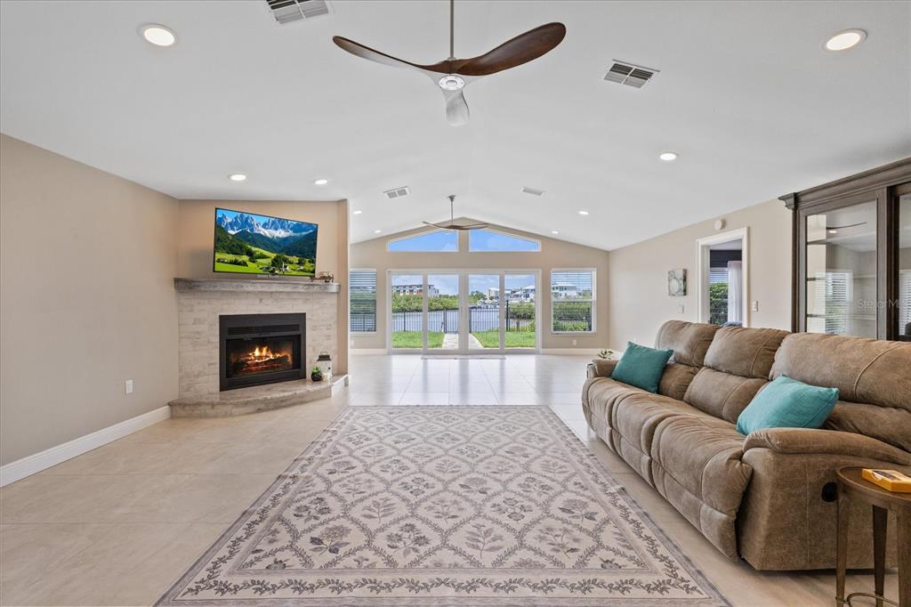 A living room features a stone fireplace, vaulted ceilings, a ceiling fan, and sliding glass doors — 4537 RICKOVER COURT, NEW PORT RICHEY, FL