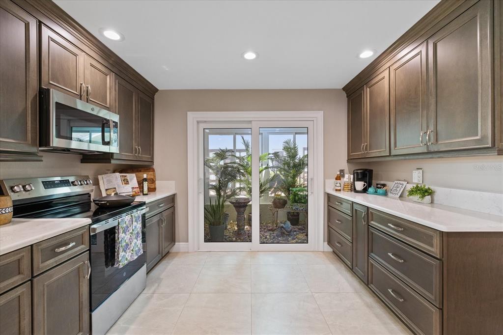 A galley kitchen features dark wood cabinets, white countertops, stainless appliances, and a sliding door — 4537 RICKOVER COURT, NEW PORT RICHEY, FL