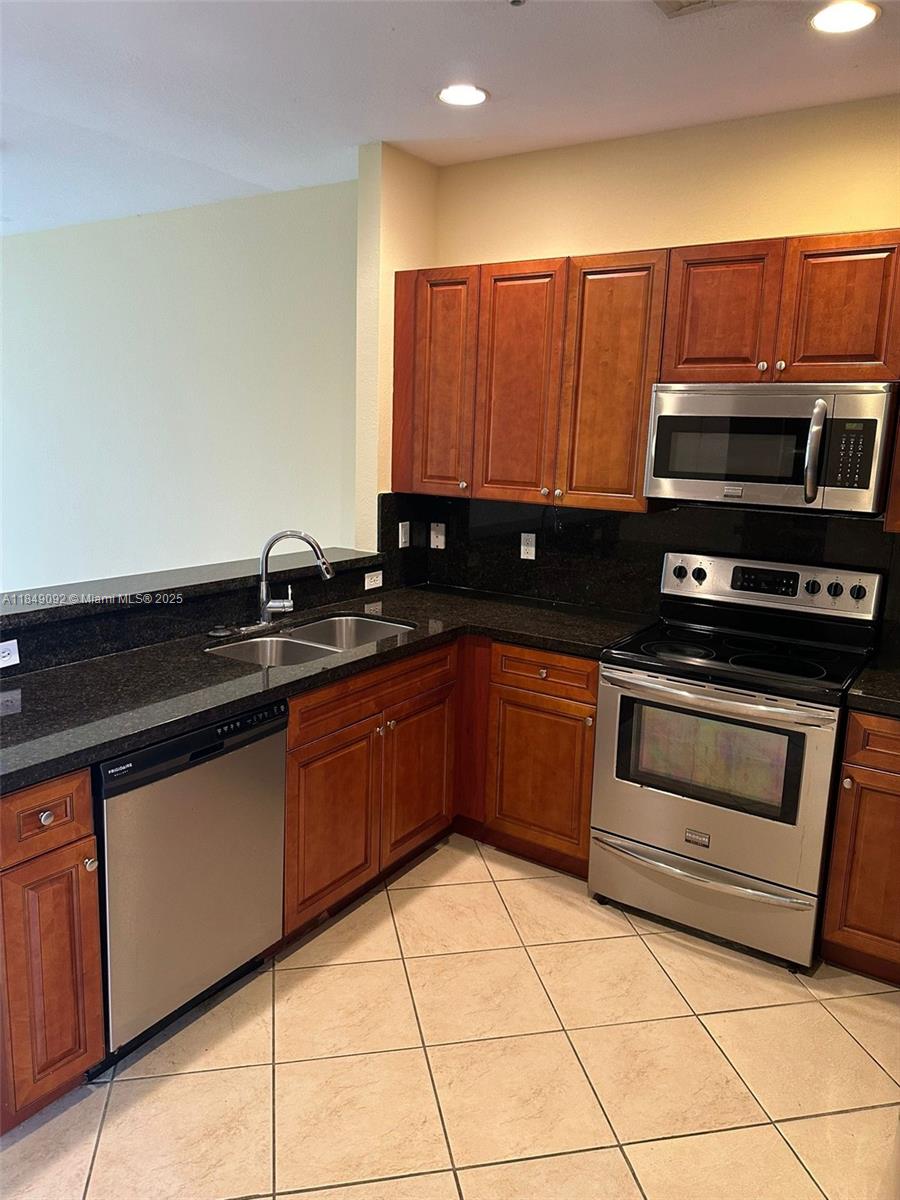 A kitchen features wood cabinets, stainless steel appliances, and dark countertops over tiled floors — 3593 NW 13th St # 3593, Lauderhill FL 33311, LAUDERHILL, FL