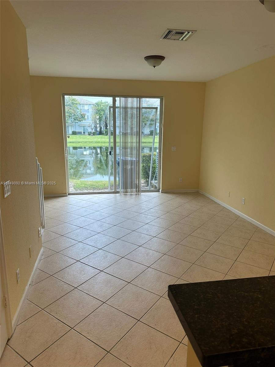 An empty room with beige tile flooring, light yellow walls, and a sliding glass door — 3593 NW 13th St # 3593, Lauderhill FL 33311, LAUDERHILL, FL