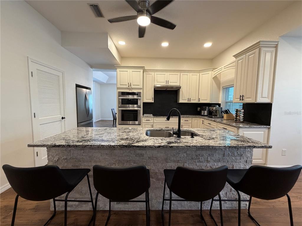 A kitchen features a stone-front island with bar stools, white cabinetry, and granite countertops — 2966 POST ROCK COURT, TARPON SPRINGS, FL