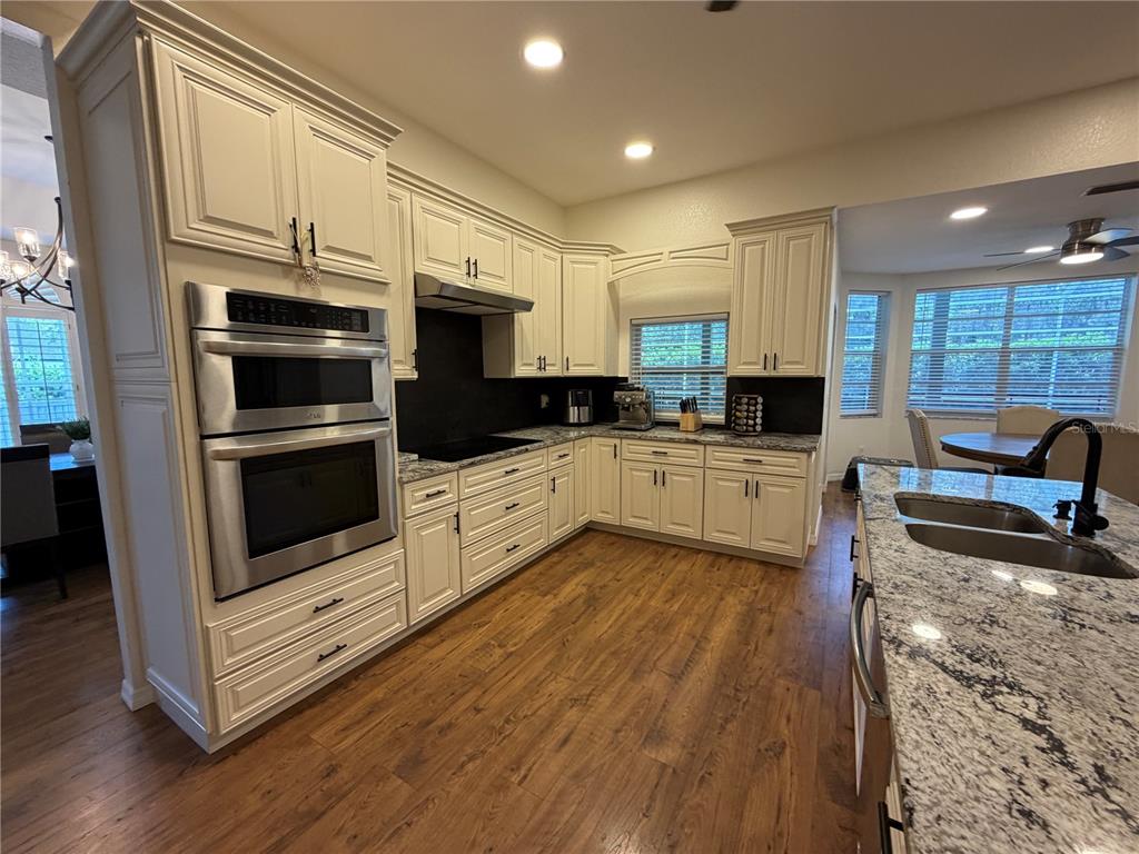 A kitchen features cream-colored cabinets, granite countertops, stainless steel appliances, and wood-look flooring — 2966 POST ROCK COURT, TARPON SPRINGS, FL