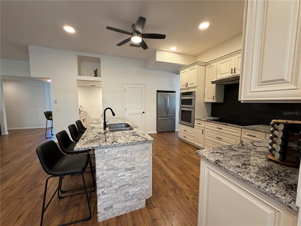 A kitchen features a stone-faced island, granite countertops, white cabinetry, and wood-look flooring — 2966 POST ROCK COURT, TARPON SPRINGS, FL