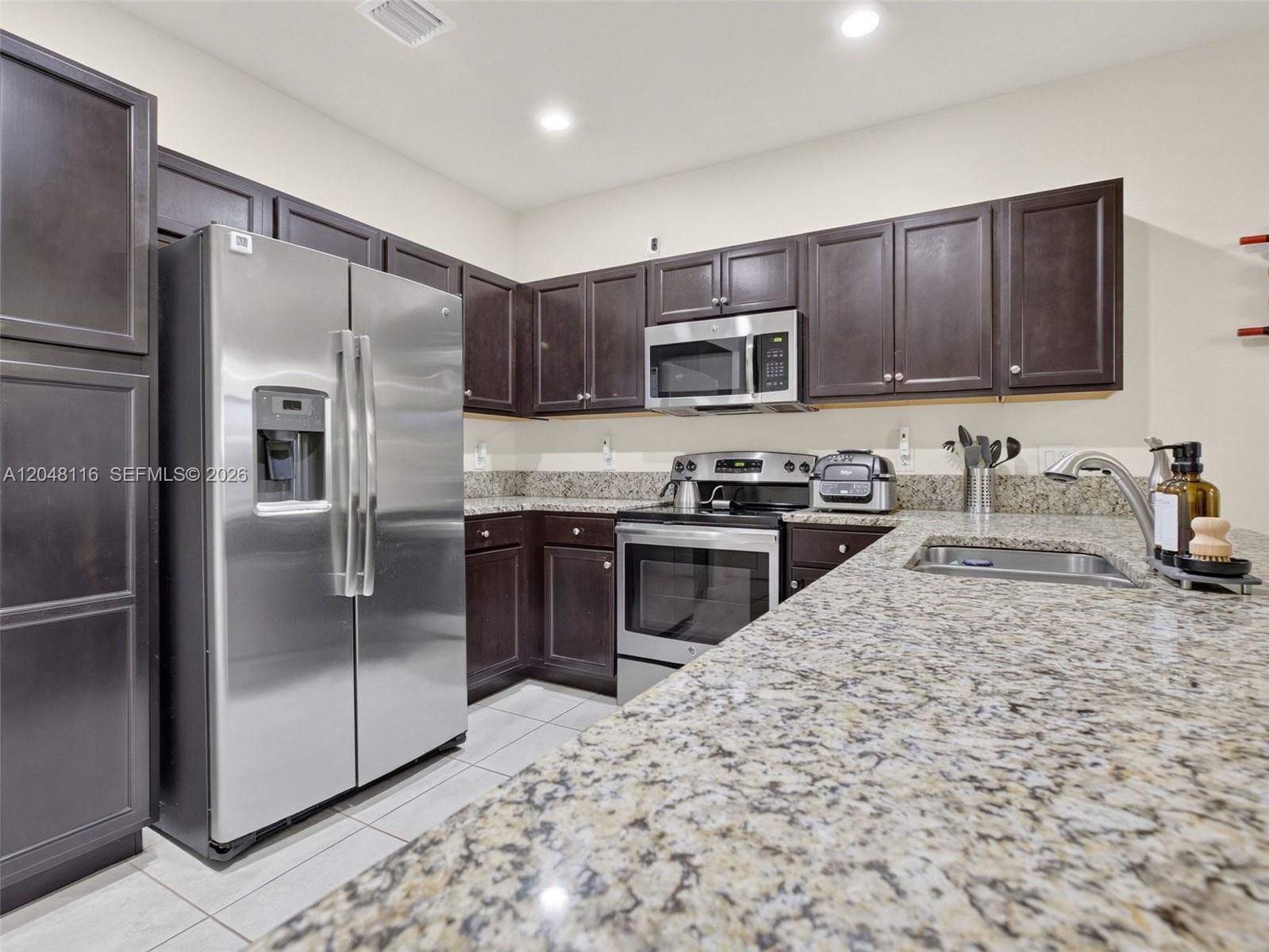 A kitchen features dark wood cabinets, granite countertops, and stainless steel appliances — 5918 NW 56th Pl, Tamarac FL 33319, TAMARAC, FL