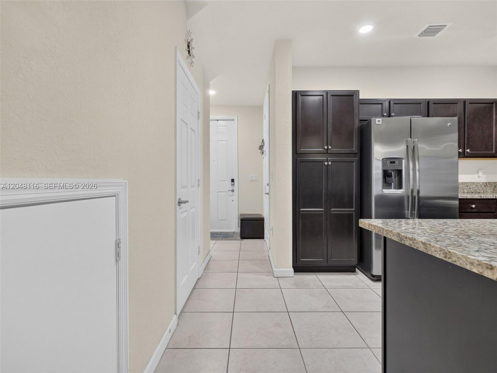 A hallway with tile flooring leads to a doorway next to dark kitchen cabinetry — 5918 NW 56th Pl, Tamarac FL 33319, TAMARAC, FL
