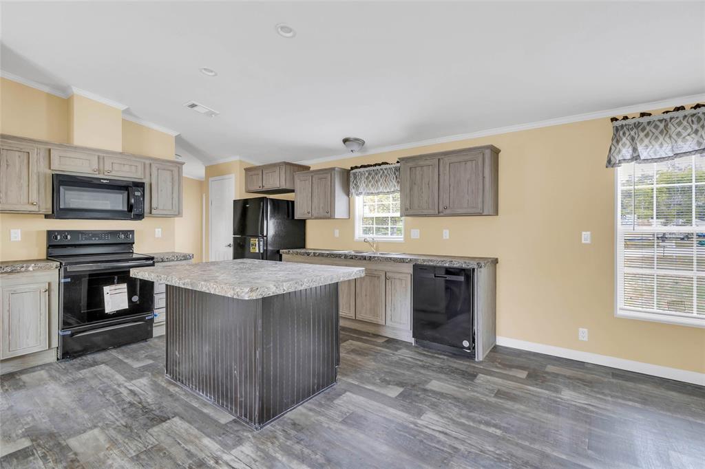 A kitchen features wood-toned cabinets, black appliances, a central island, and wood-look flooring — 7193 SEALAWN DRIVE, SPRING HILL, FL