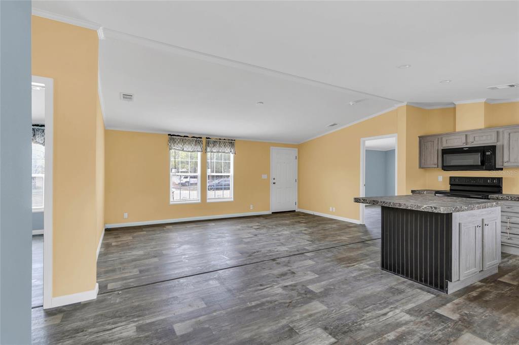 An open-concept living area features yellow walls, wood-look flooring, and a kitchen with an island — 7193 SEALAWN DRIVE, SPRING HILL, FL