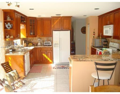 A kitchen features wood cabinets, granite countertops, a white refrigerator, and a breakfast bar — 5273 NW 113th Ave, Doral FL 33178, DORAL, FL