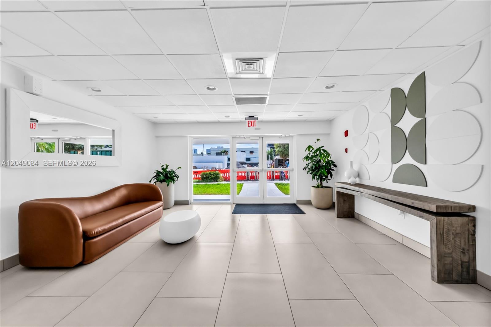 A modern lobby features a brown sofa, a wooden console table, and glass entry doors — 1666 West Ave # 404, Miami Beach FL 33139, MIAMI BEACH, FL