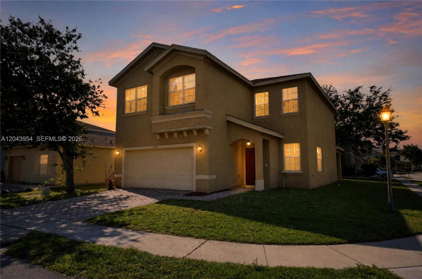 A two-story tan stucco house with a two-car garage and a paved driveway at sunset — 9317 Natures Way, Fort Pierce FL 34945, FORT PIERCE, FL