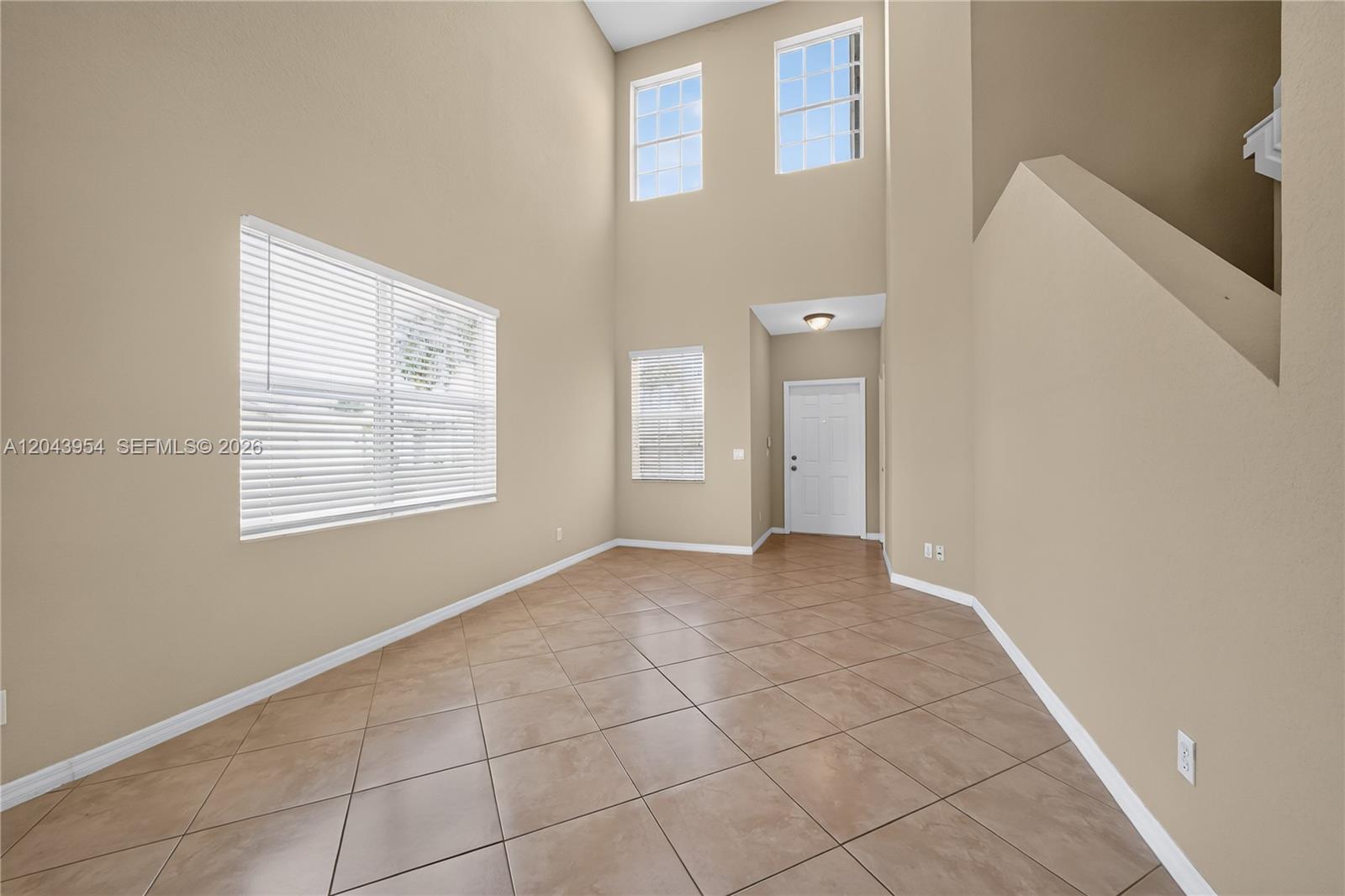 A high-ceilinged room features beige walls, tile flooring, and several windows with white blinds — 9317 Natures Way, Fort Pierce FL 34945, FORT PIERCE, FL