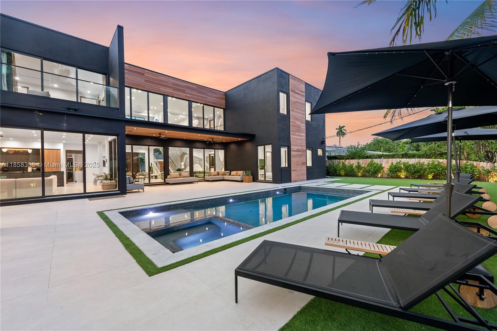 A modern two-story house with a swimming pool, patio, and lounge chairs at dusk — 1960 NE 197th Ter, Miami FL 33179, MIAMI, FL