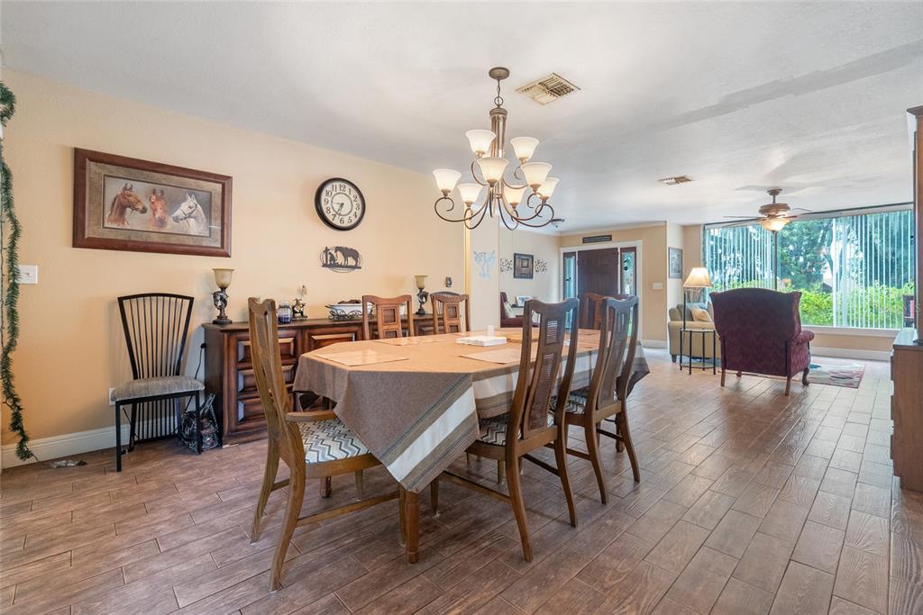 A dining room with a wooden table, chairs, chandelier, and tile flooring leads into a living area — 306 GRIMES DRIVE, AUBURNDALE, FL