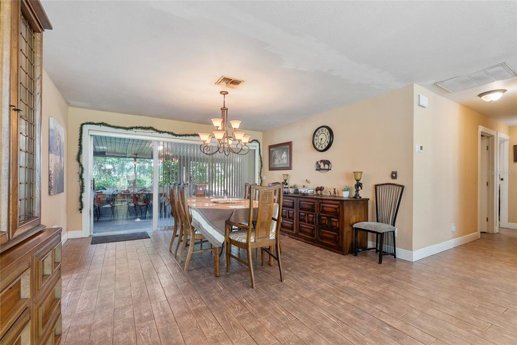 A dining room features wood-look tile flooring, a chandelier, a wooden table, and sliding doors — 306 GRIMES DRIVE, AUBURNDALE, FL
