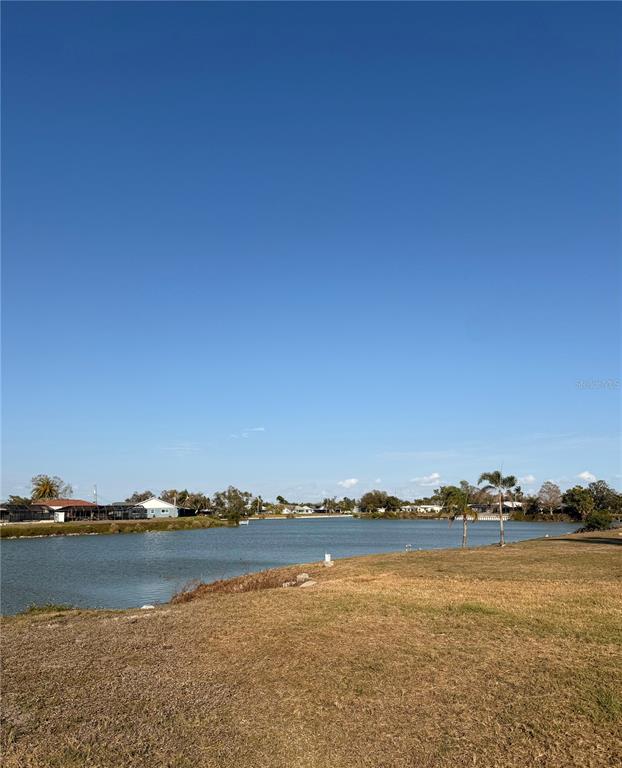 A grassy lawn overlooks a calm lake with houses visible along the distant shore — 303 SHAMROCK BOULEVARD, VENICE, FL