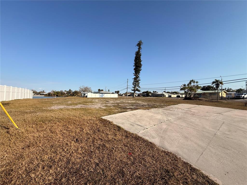 A vacant lot features a concrete slab, dry grass, and a tall tree under clear skies — 303 SHAMROCK BOULEVARD, VENICE, FL