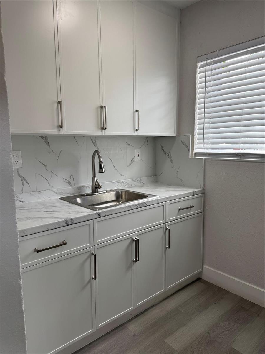 A kitchen area features white cabinets, a stainless steel sink, and marble-patterned countertops and backsplash — 731 NW 56th Street, Miami FL 33127, MIAMI, FL