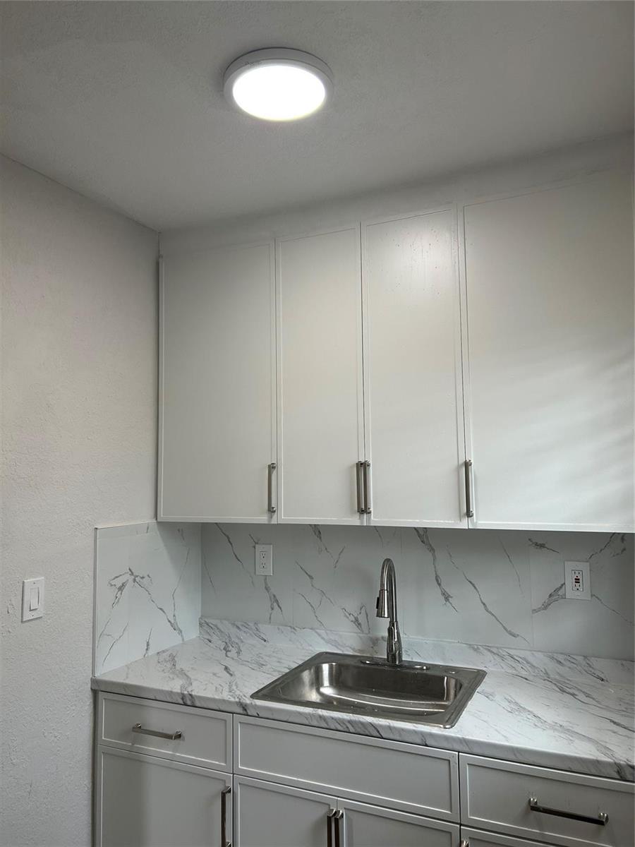 A kitchen sink area features white cabinets, marble-patterned countertops, and a matching backsplash — 731 NW 56th Street, Miami FL 33127, MIAMI, FL