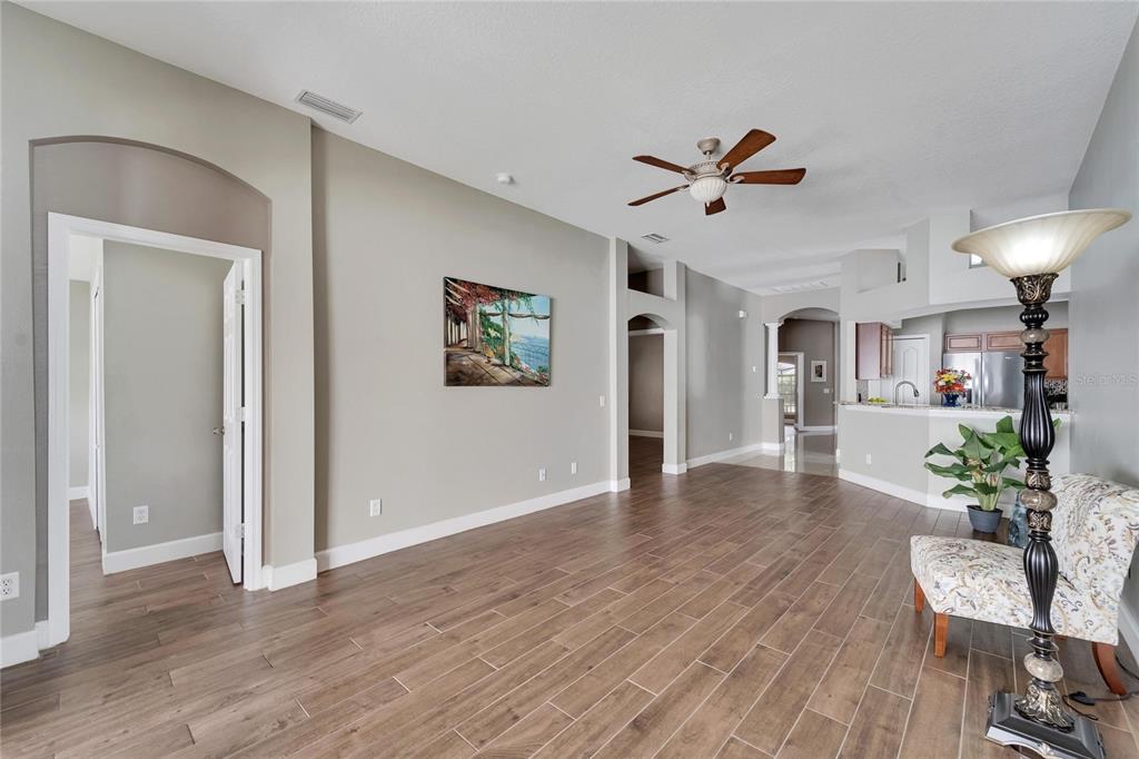An open-concept living area features wood-look tile flooring, neutral walls, and a ceiling fan — 12739 STANDBRIDGE DRIVE, RIVERVIEW, FL