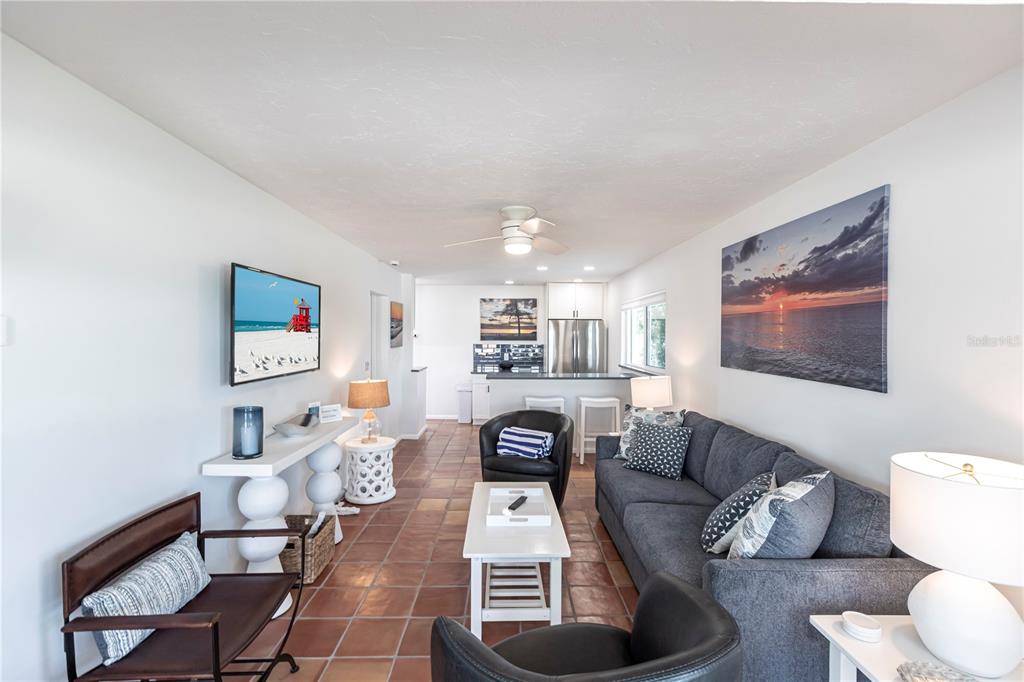 A living room with tile floors, a gray sofa, two black armchairs, and a kitchen — 6020 MIDNIGHT PASS ROAD UNIT 48, SARASOTA, FL