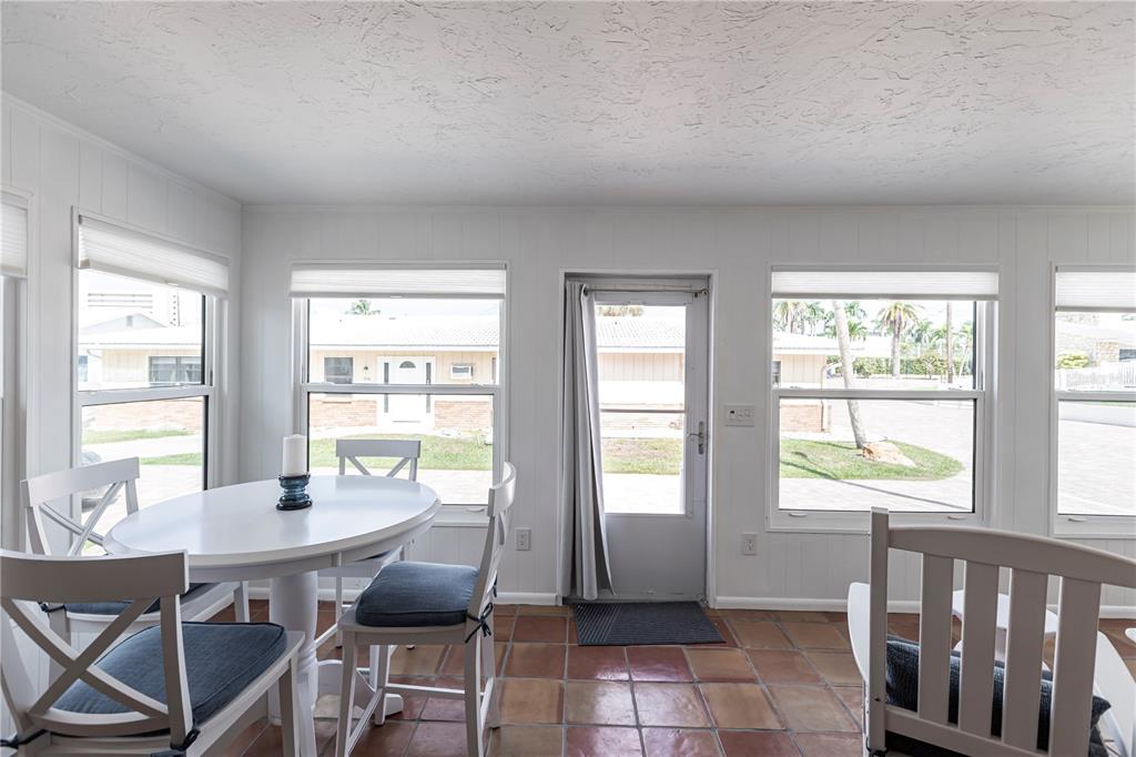 A sunroom features white paneled walls, a round dining table, and terracotta tile flooring — 6020 MIDNIGHT PASS ROAD UNIT 48, SARASOTA, FL