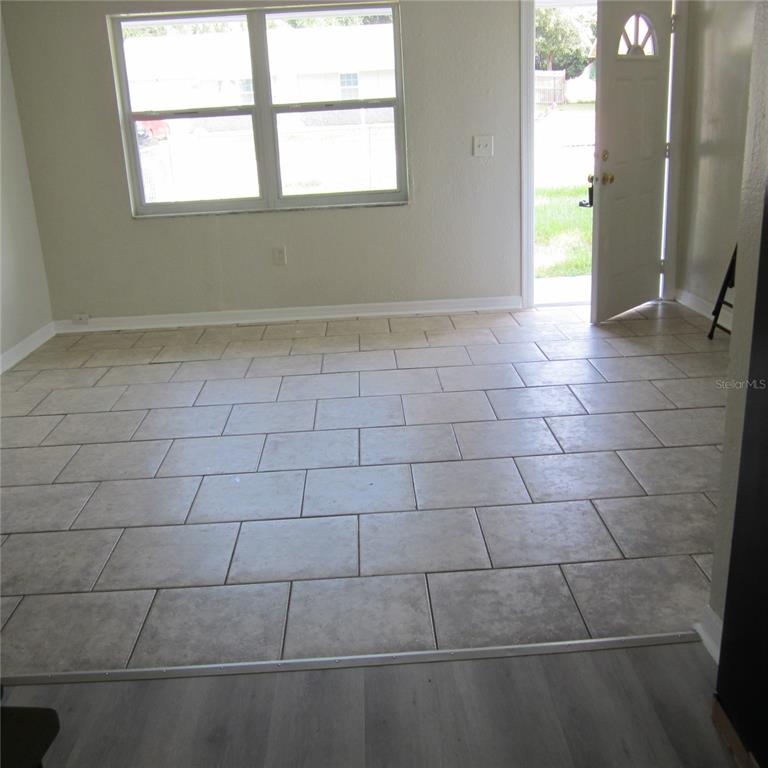 A room with light-colored tile flooring, a large window, and an open exterior door — 520 W ELLA J GILMORE STREET, APOPKA, FL