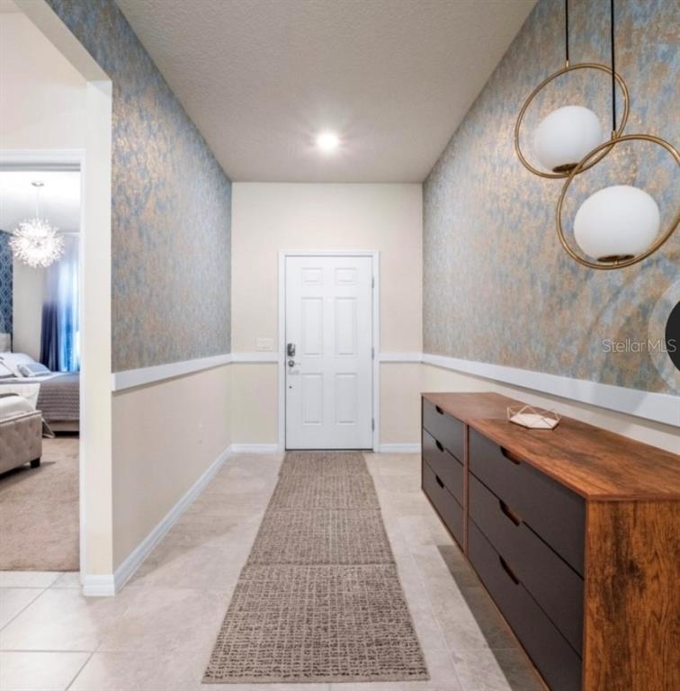 A hallway features textured blue and gold wallpaper, a wood dresser, and modern pendant lighting — 2031 LELANI CIRCLE, DAVENPORT, FL