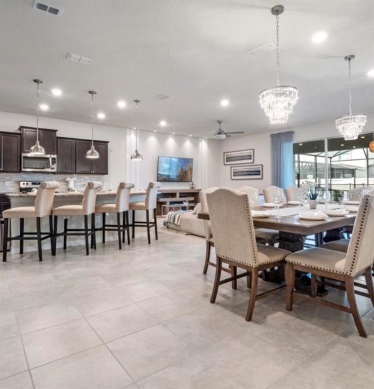 An open-concept kitchen and dining area features dark cabinetry, pendant lighting, and tile flooring — 2031 LELANI CIRCLE, DAVENPORT, FL
