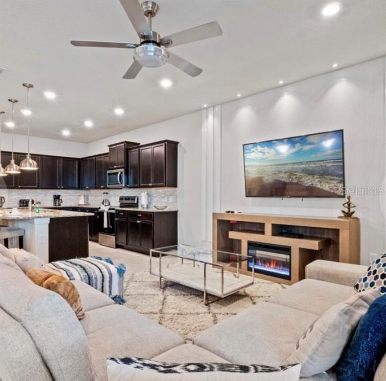 An open-concept living room and kitchen featuring dark cabinetry, a ceiling fan, and a fireplace — 2031 LELANI CIRCLE, DAVENPORT, FL
