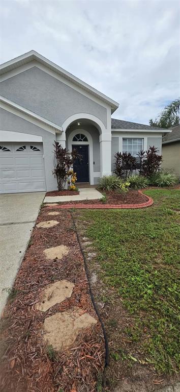 A gray house exterior features a dark blue front door, a garage, and a stone walkway — 3233 DOWNAN POINT DRIVE, LAND O LAKES, FL