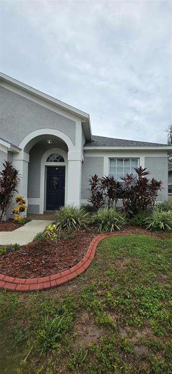 A gray stucco house features a dark front door, arched entryway, and a landscaped front yard — 3233 DOWNAN POINT DRIVE, LAND O LAKES, FL
