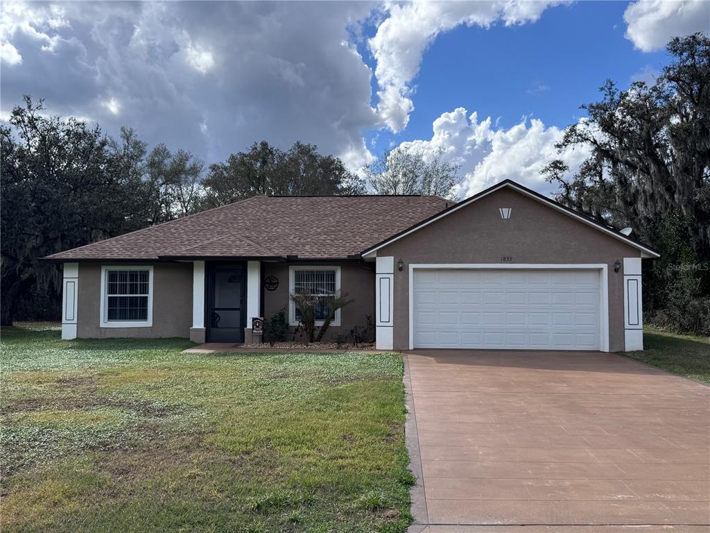 A single-story house with a brown stucco exterior, a two-car garage, and a concrete driveway — 1855 N BERKLEY ROAD, AVON PARK, FL