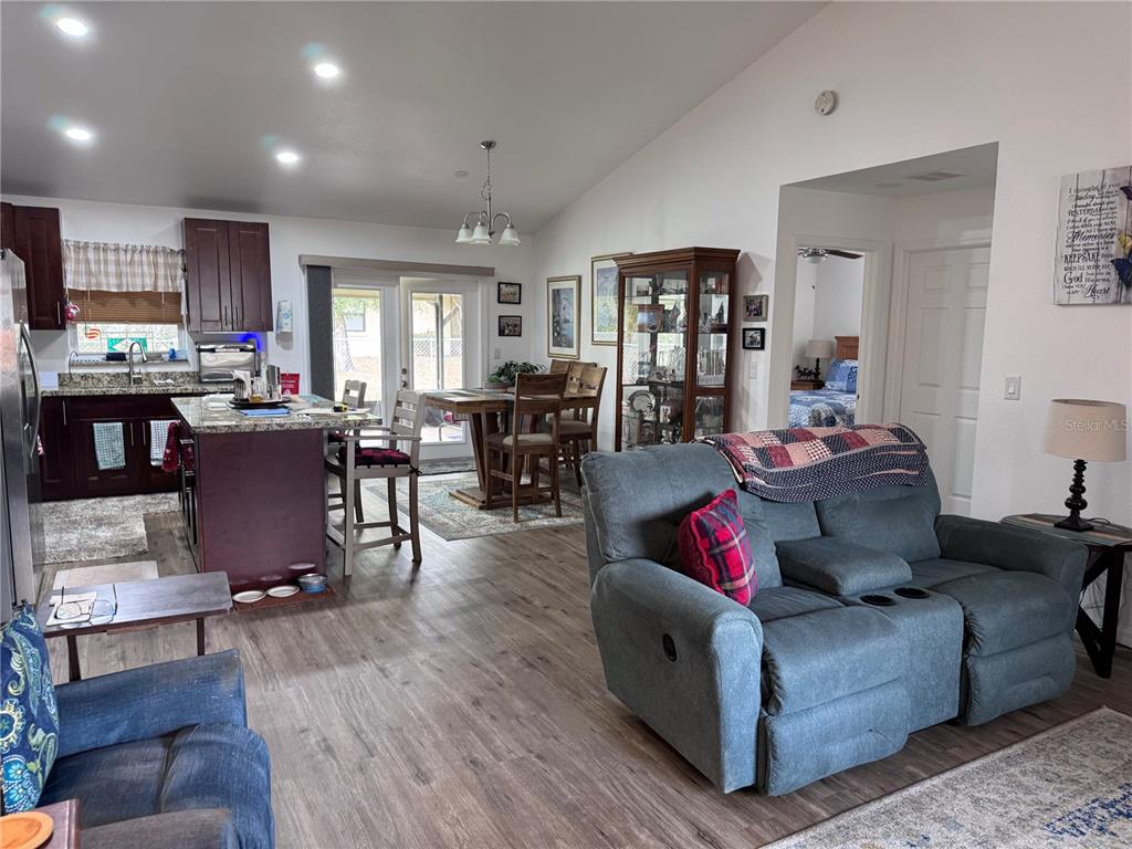 An open-concept living room and kitchen area features wood-look flooring and a gray reclining sofa — 1855 N BERKLEY ROAD, AVON PARK, FL