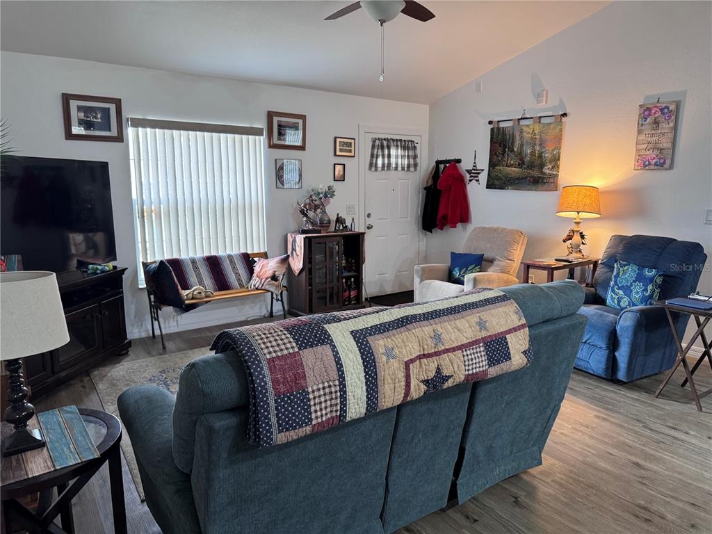 A living room features a blue sofa, two recliners, a window with blinds, and wood-look flooring — 1855 N BERKLEY ROAD, AVON PARK, FL
