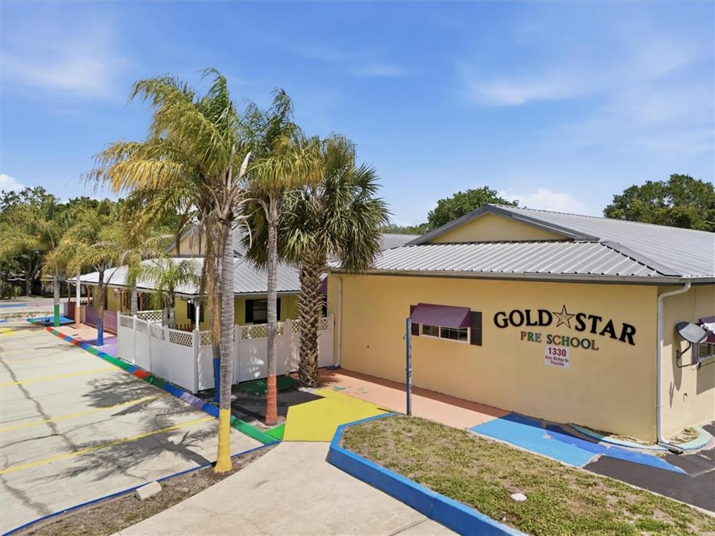 An exterior view of a yellow preschool building with palm trees and a paved parking area — 1330 KNOX MC RAE DRIVE UNIT 6A, TITUSVILLE, FL