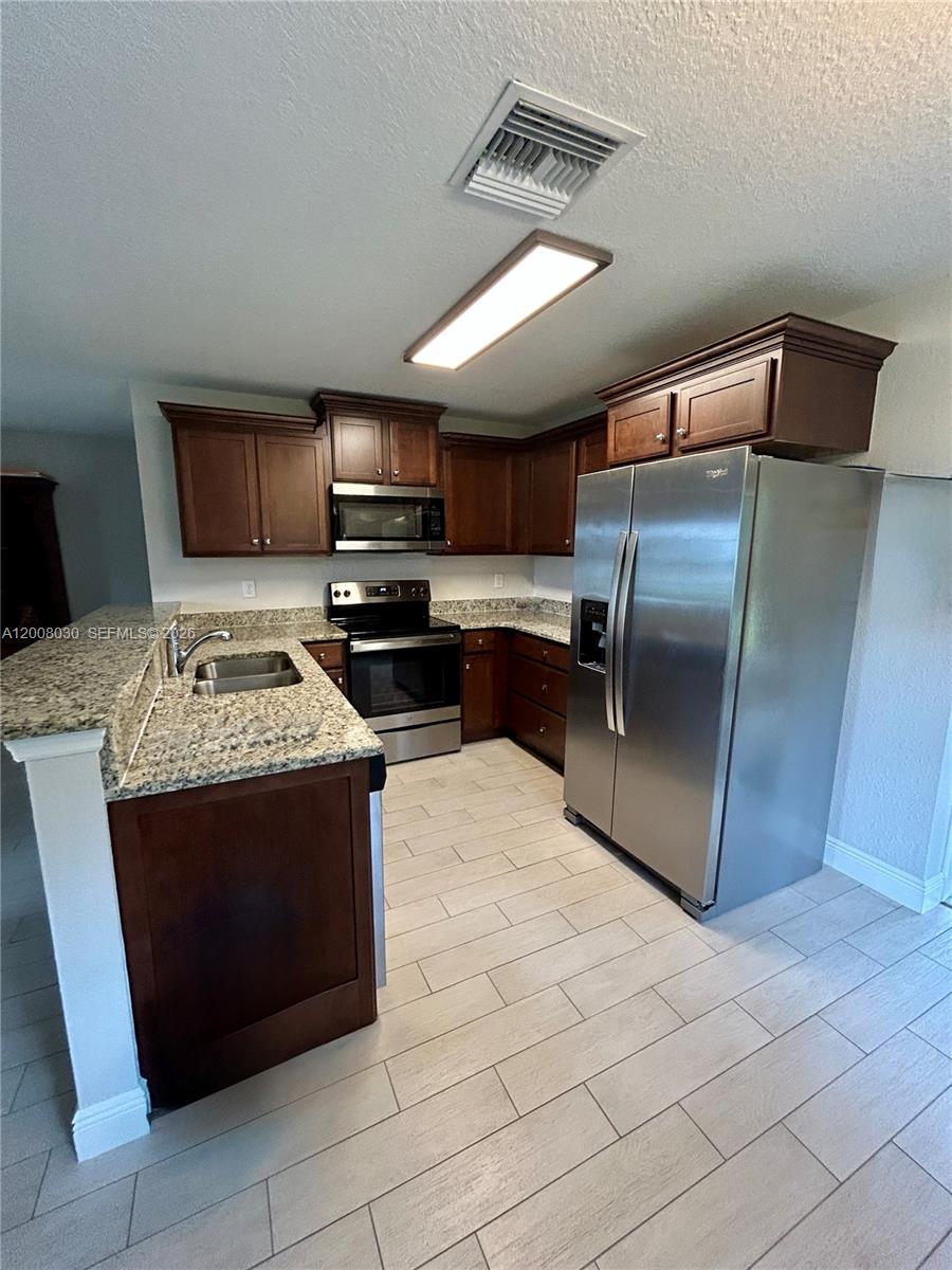 A kitchen features dark wood cabinets, granite countertops, stainless steel appliances, and light tile flooring — 358 Lime Rd NW, Lake Placid FL 33852, LAKE PLACID, FL