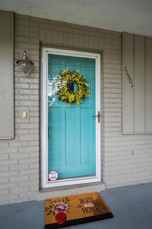 A teal front door with a yellow wreath sits in a light gray brick wall — 11501 119TH TERRACE, LARGO, FL