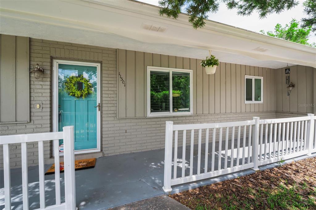 A covered porch with a teal front door, white railings, and gray brick siding — 11501 119TH TERRACE, LARGO, FL