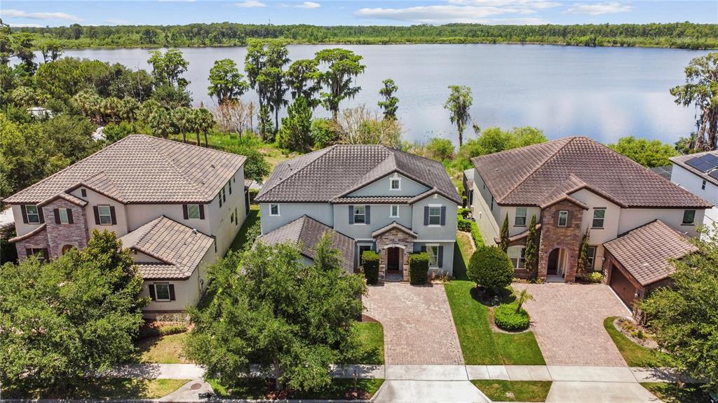 An aerial view shows three suburban houses with tiled roofs situated along a lakefront — 8394 LOOKOUT POINTE DRIVE, WINDERMERE, FL