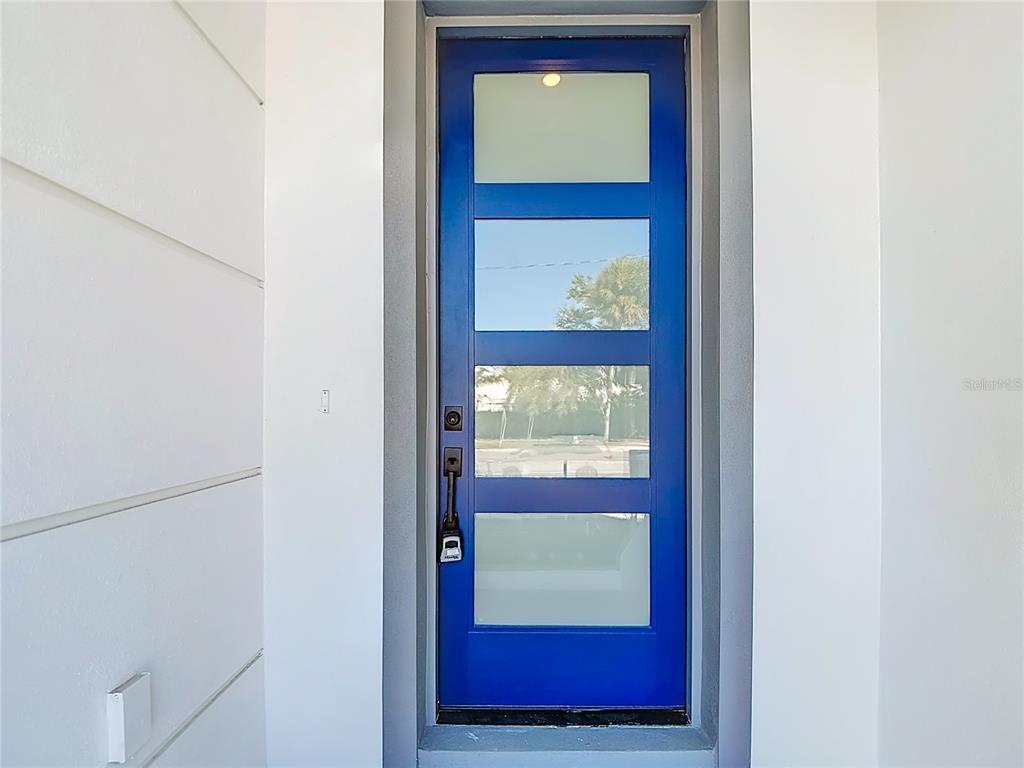 A bright blue modern front door with four glass panels sits in a white entryway — 410 S WEST SHORE BOULEVARD, TAMPA, FL