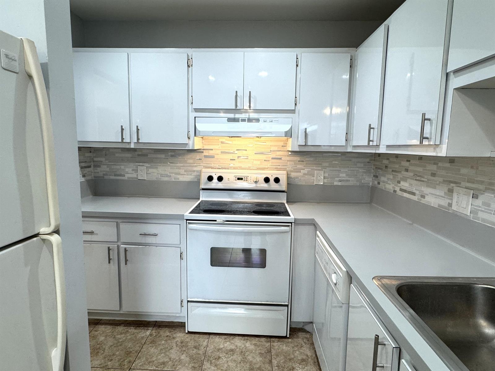 A kitchen features white cabinets, a white stove, a tiled backsplash, and gray countertops — 1100 Boxwood Drive # 101, Delray Beach FL 33445, DELRAY BEACH, FL